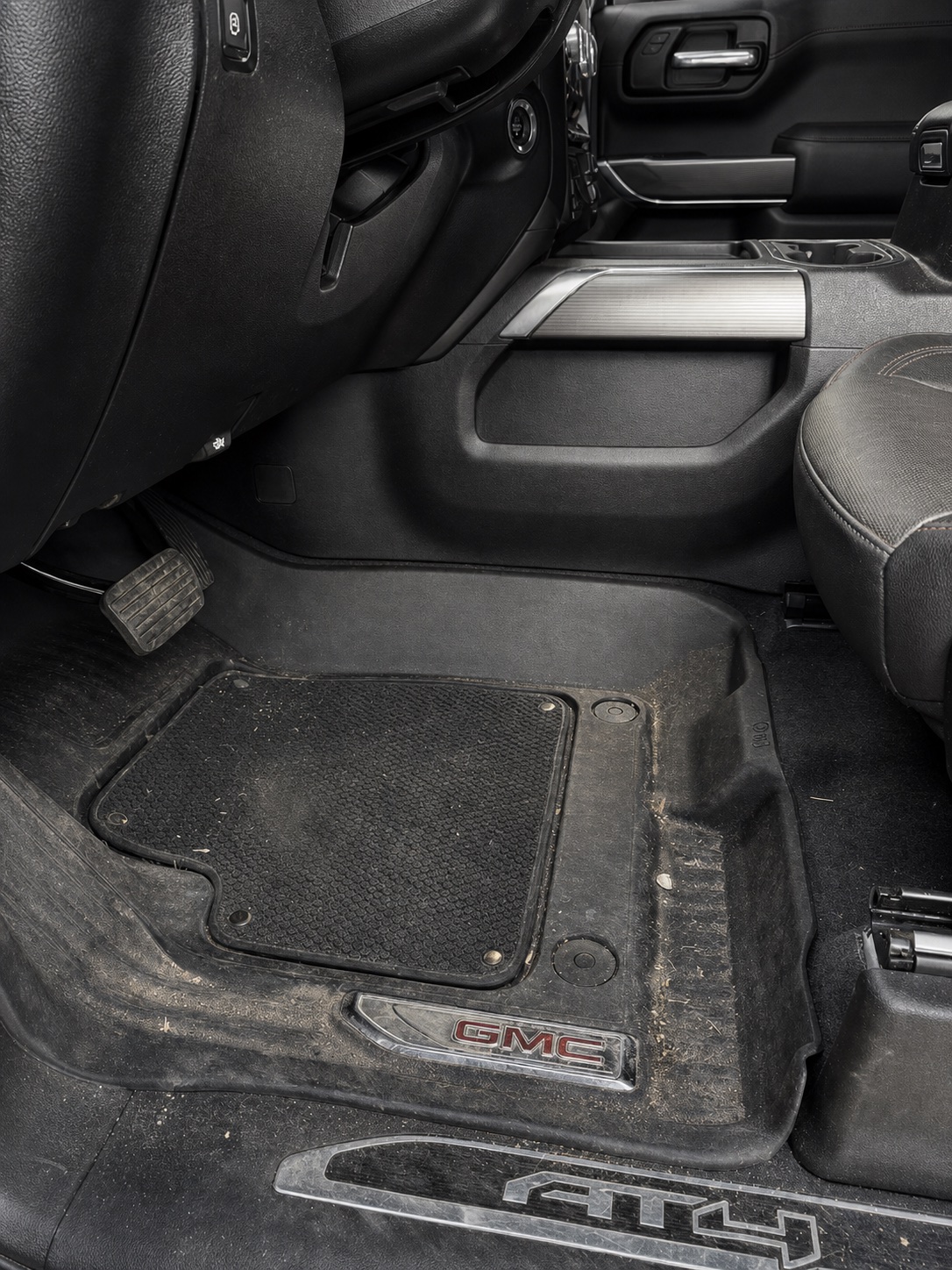 Driver footwell before an interior detail, with visible dirt on the floor mat